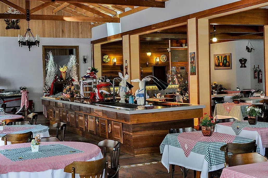 O salão do restaurante do hotel, em madeira, com toalhas xadrez e o balcão ao fundo